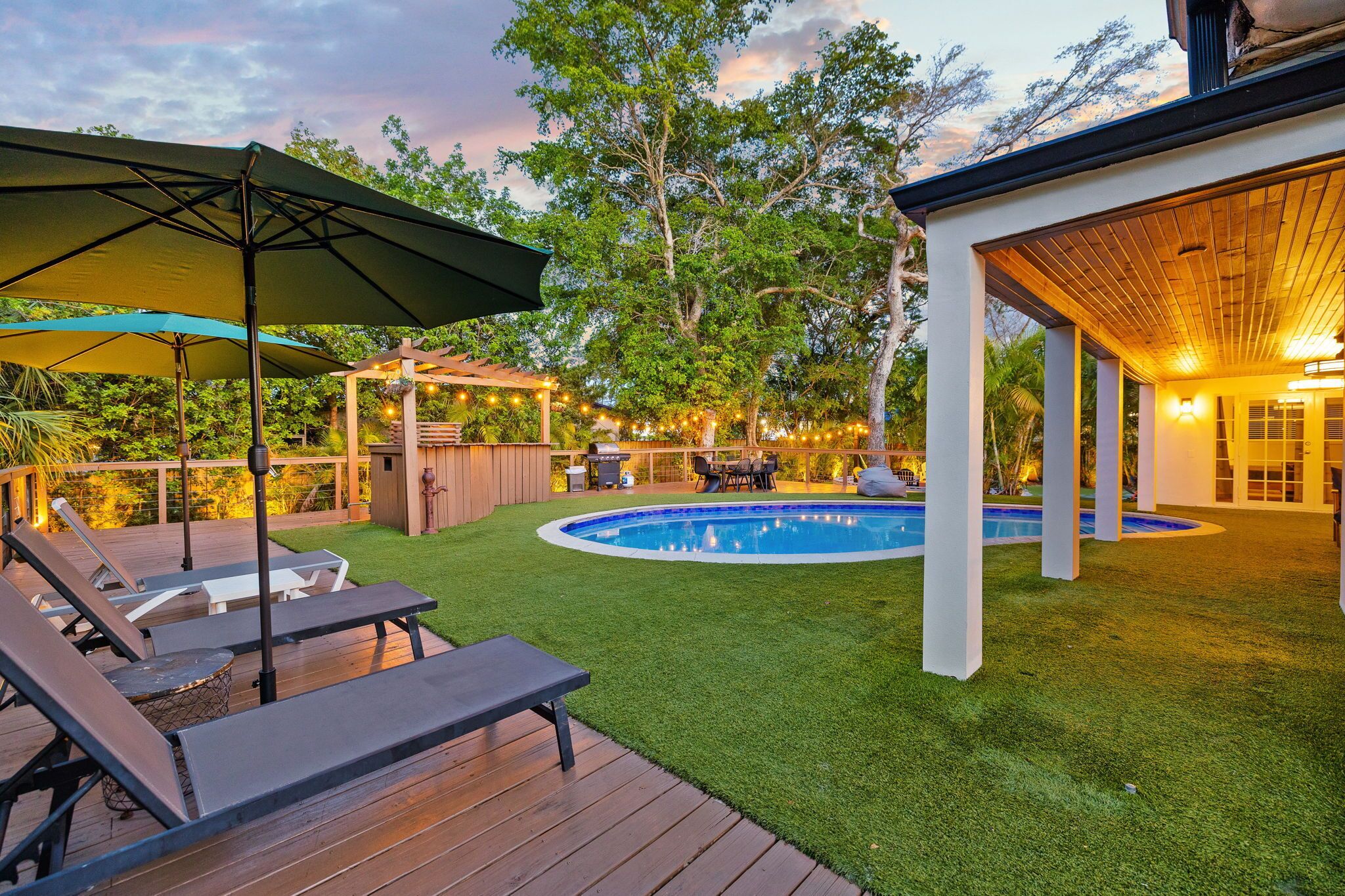 A backyard with a pool, lounge chairs, and a covered patio area.