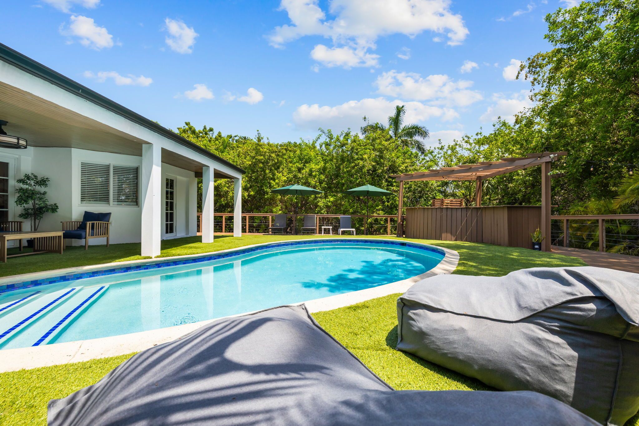Una piscina con muelle de madera, mobiliario exterior y zona de estar techada.