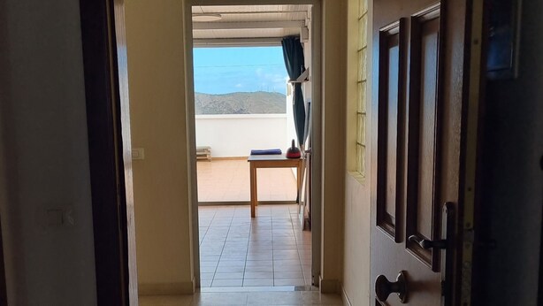 Ein Flur mit Zugang zu einem Balkon und Blick, einer Holztür und einem gefliesten Boden.