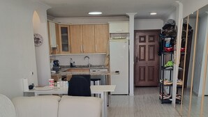 Ein modernes Wohnzimmer mit einer Couch, einem Glastisch und einem Küchenbereich im Hintergrund.