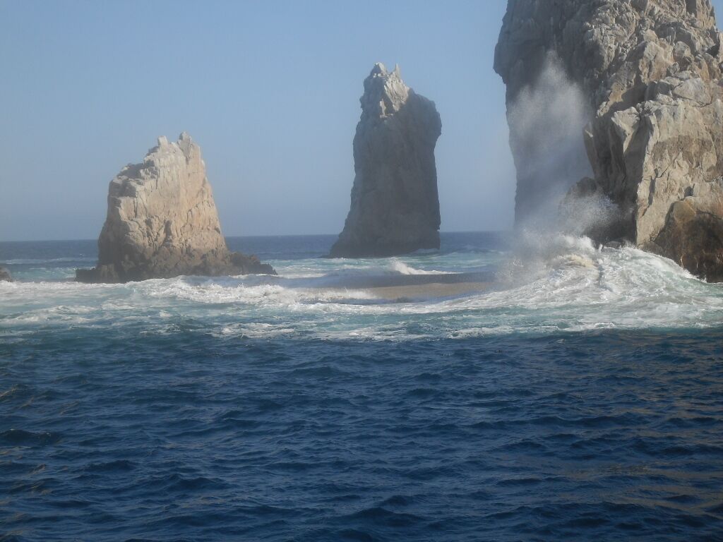 A coastal scene with two prominent rock formations in the sea, waves crashing against them, and a clear sky.