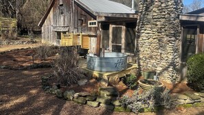 A rustic cabin with a stone chimney, a metal hot tub, and a wooden deck.