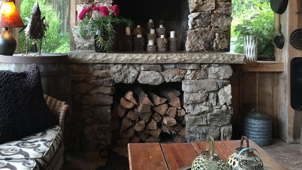 A rustic interior with a stone fireplace, a wooden bench, and a table with decorative lanterns.
