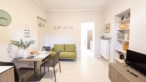 A modern living room with a dining area, a green sofa, a wooden dining table, and a television on a wooden cabinet. - Courtyard & Balconies (Como)