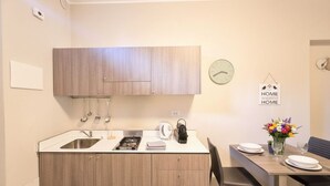 A compact kitchen with wooden cabinets, a sink, a stove, and a dining area with a table set for two. - Courtyard & Balconies (Como)