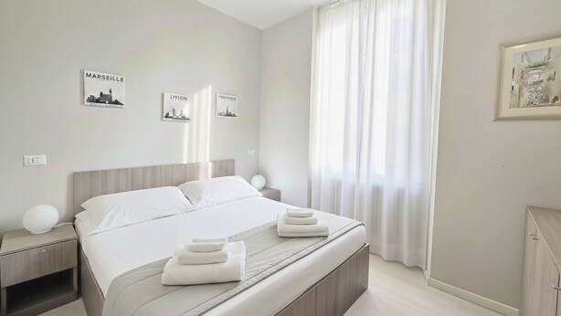 A minimalist hotel room with a large bed, white bedding, and a cityscape artwork on the wall. - Courtyard & Balconies (Como)
