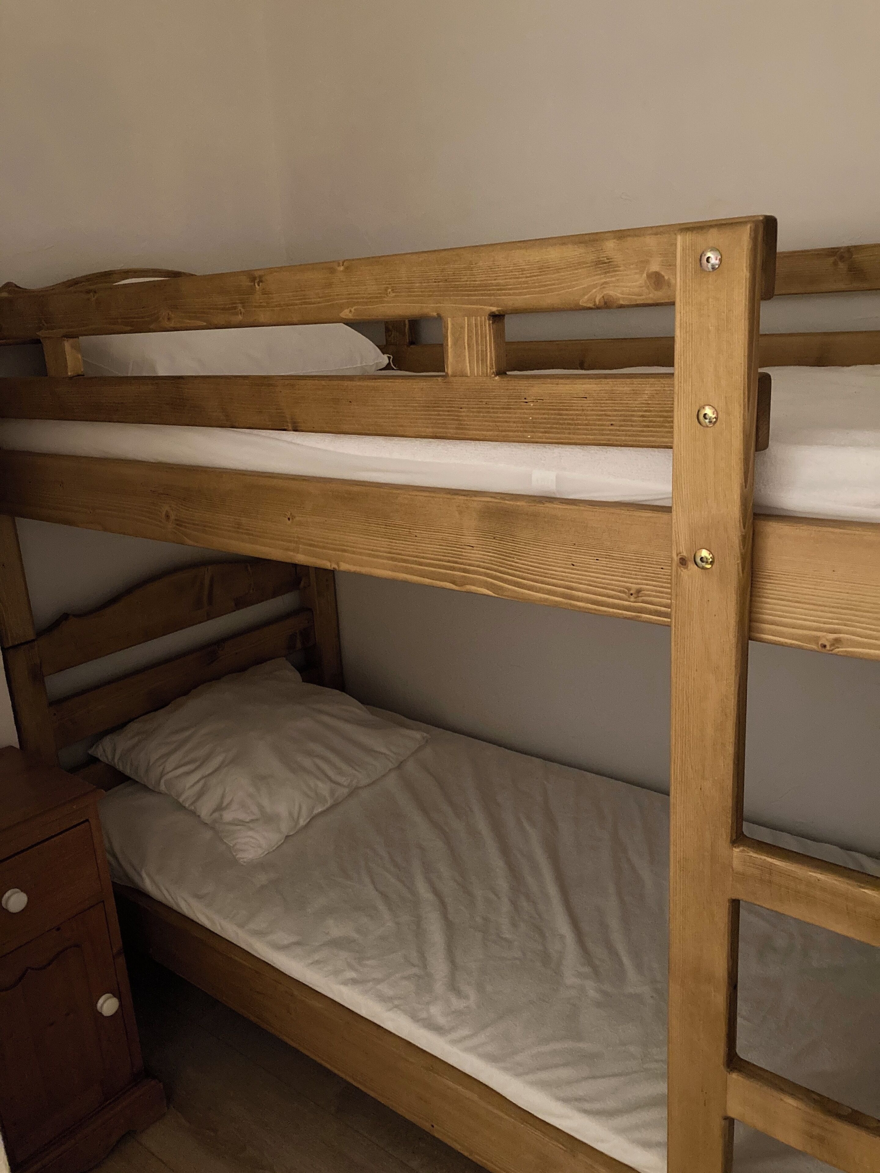 A bunk bed with a wooden frame and white bedding.