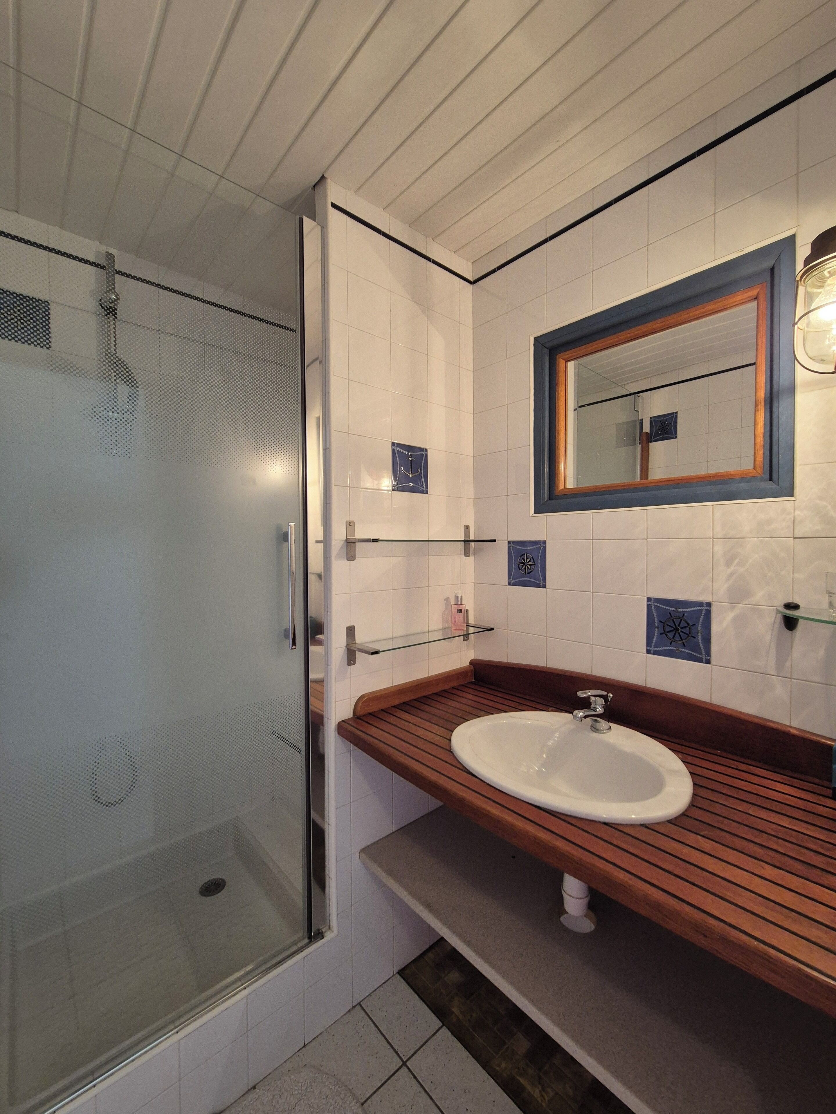 A modern bathroom with a glass shower enclosure, a wooden vanity, and a large mirror with a wooden frame.