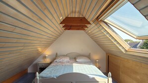 A bedroom with a sloped ceiling, a skylight, a bed, bedside tables, and a nightstand.
