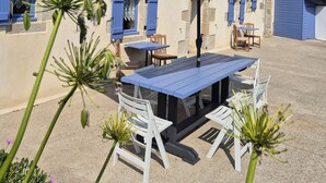 A building with stone walls and blue shutters, a patio with a table and chairs, and a large umbrella.