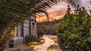 Un chemin sinueux mène à un bâtiment, avec un paysage désertique et un coucher de soleil en arrière-plan.