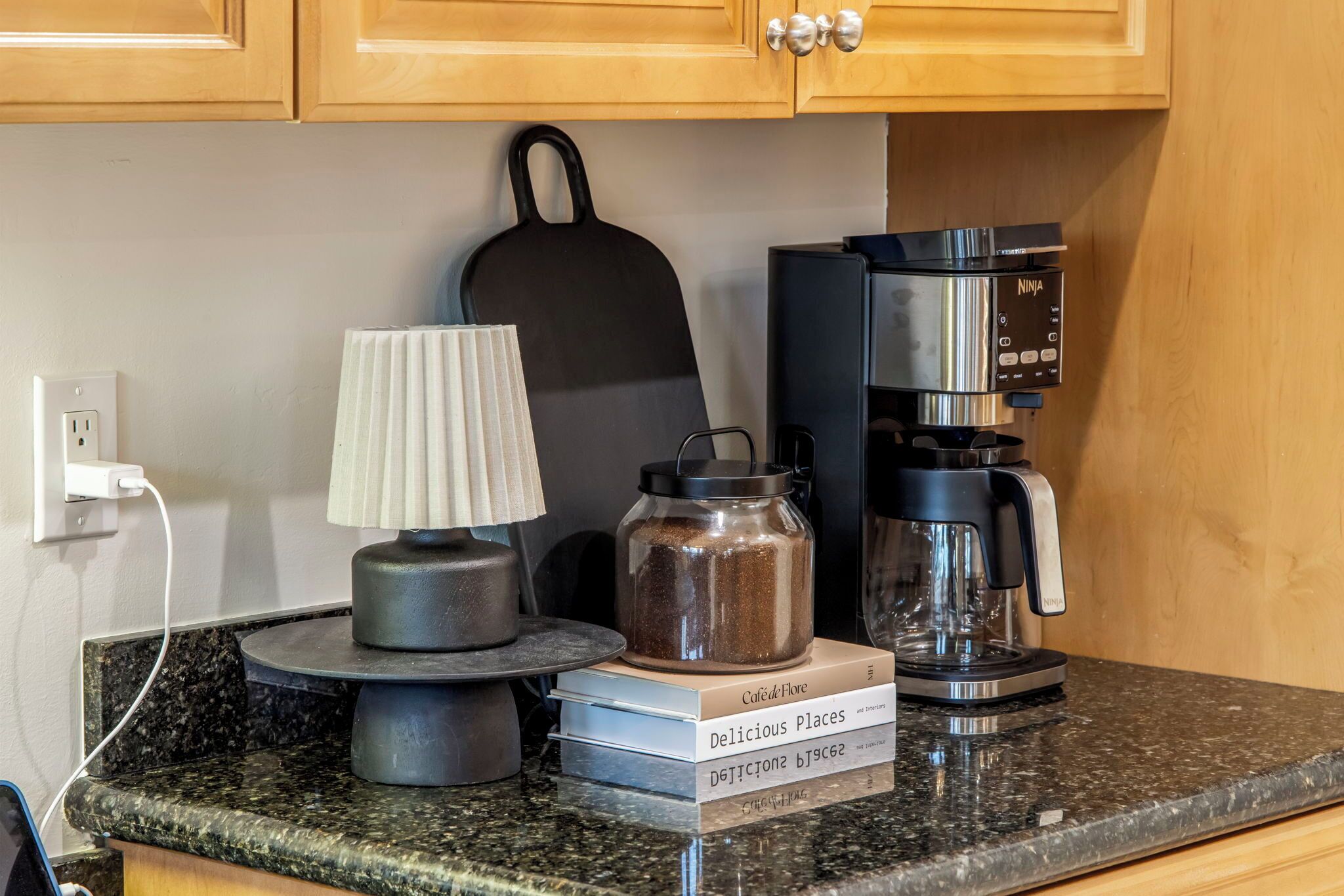 A kitchen counter with a coffee maker, a kettle, a jar, a lamp, and a few books.