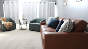 Een woonkamer met een bruine leren bank, twee groene fauteuils en een kleine tafel.