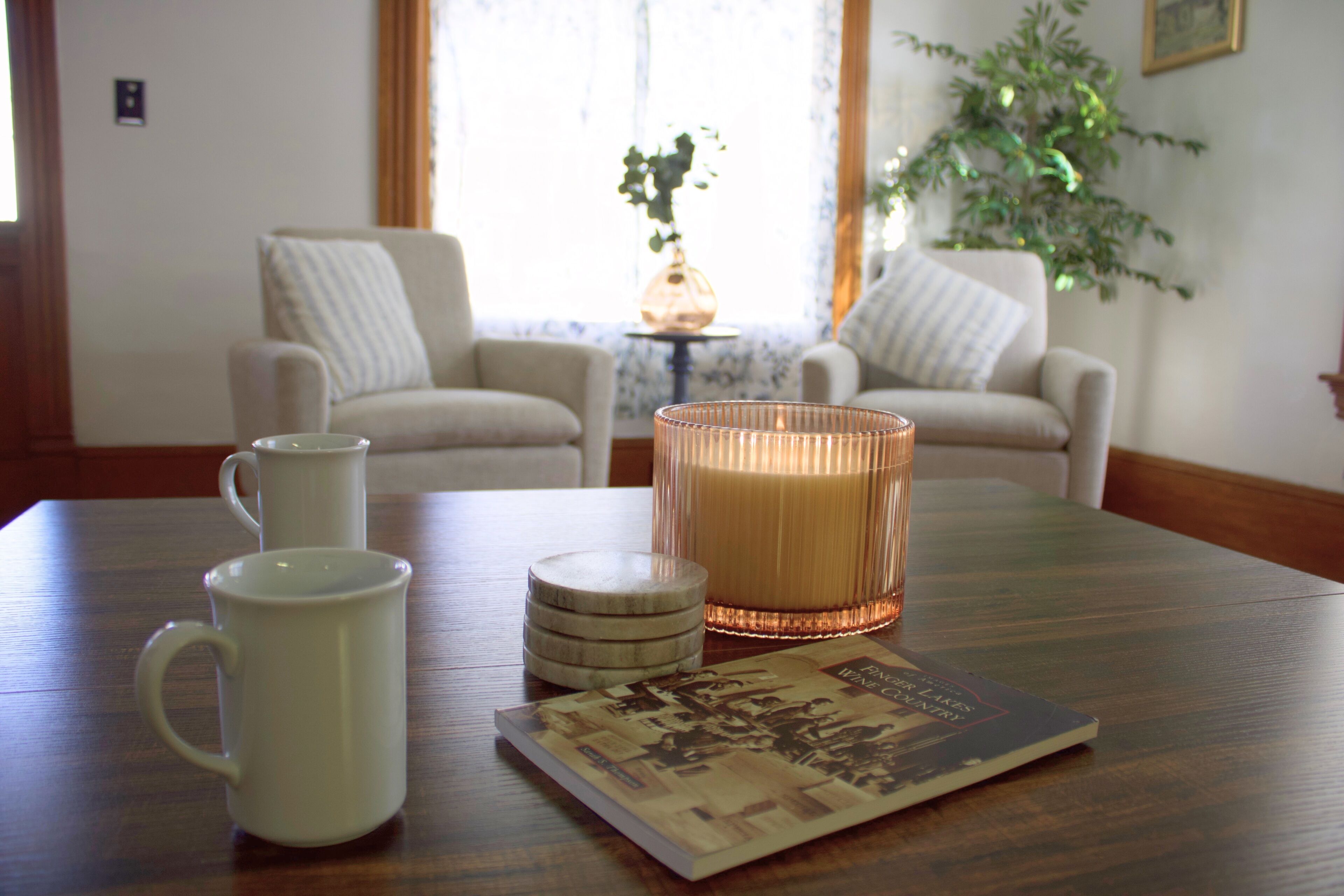 Ein Zimmer mit einem Holztisch, zwei weißen Stühlen, einer Kerze und einem Buch.