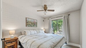 A bedroom with a bed, nightstand, lamp, ceiling fan, and a window with curtains. - Walk to Shops Restaurants Coffee Live Music (Cave Creek)