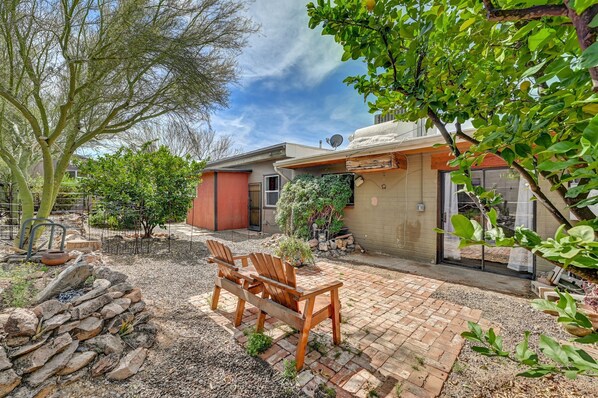 A patio area with wooden chairs, a stone fire pit, and a small garden with potted plants and a tree.