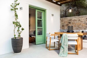 Una habitació amb una porta verda, una planta en test, una taula de fusta amb cadires i una paret de pedra.