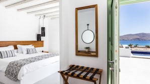 A bedroom with a bed, a bedside table, a mirror, and a view of the sea. - Suite with Private Pool and sea view (Mykonos)