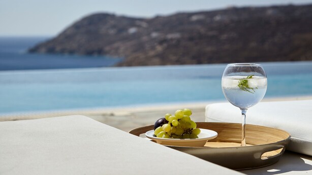A tray with a glass of water and a bowl of grapes on a beach with a view of the sea and a mountain in the background. - Amazing view Mykonian Villa with 5 bedrooms and pool (Mykonos)
