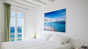 A bedroom with a bed, a nightstand, a lamp, and a view of the sea through a window. - Amazing view Mykonian Villa with 5 bedrooms and pool (Mykonos)