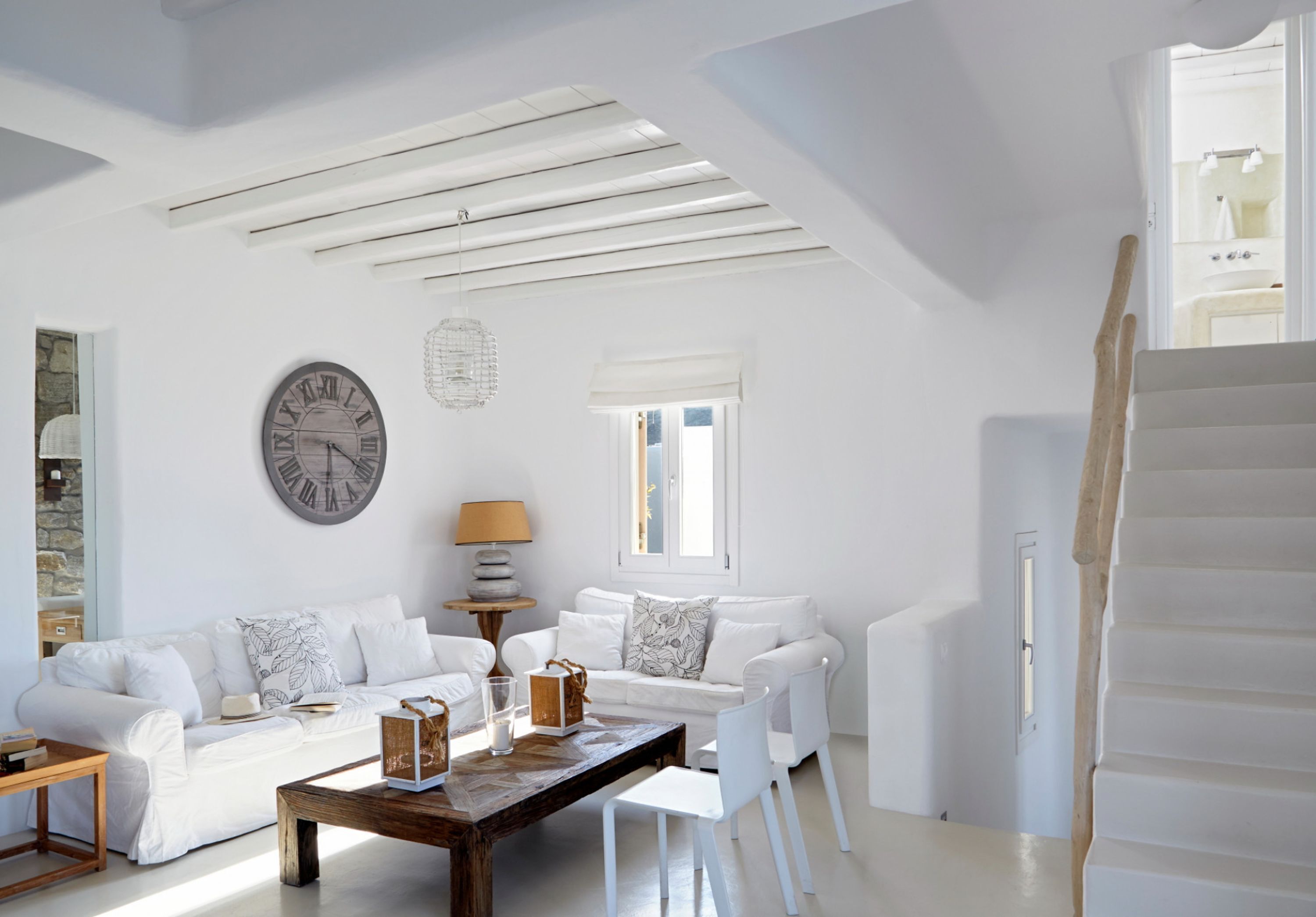 Un salon spacieux avec un ensemble de canapés blancs, une table basse en bois et une grande horloge murale.