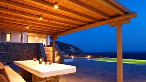 An outdoor bar area with a stone table, wooden beams, and a view of the sea at dusk. - Amazing view Mykonian Villa with 5 bedrooms and pool (Mykonos)