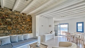 A modern living room with a stone wall, a wooden coffee table, and a sofa with striped cushions. - 2 Bedroom Villa with private pool (Panormos)