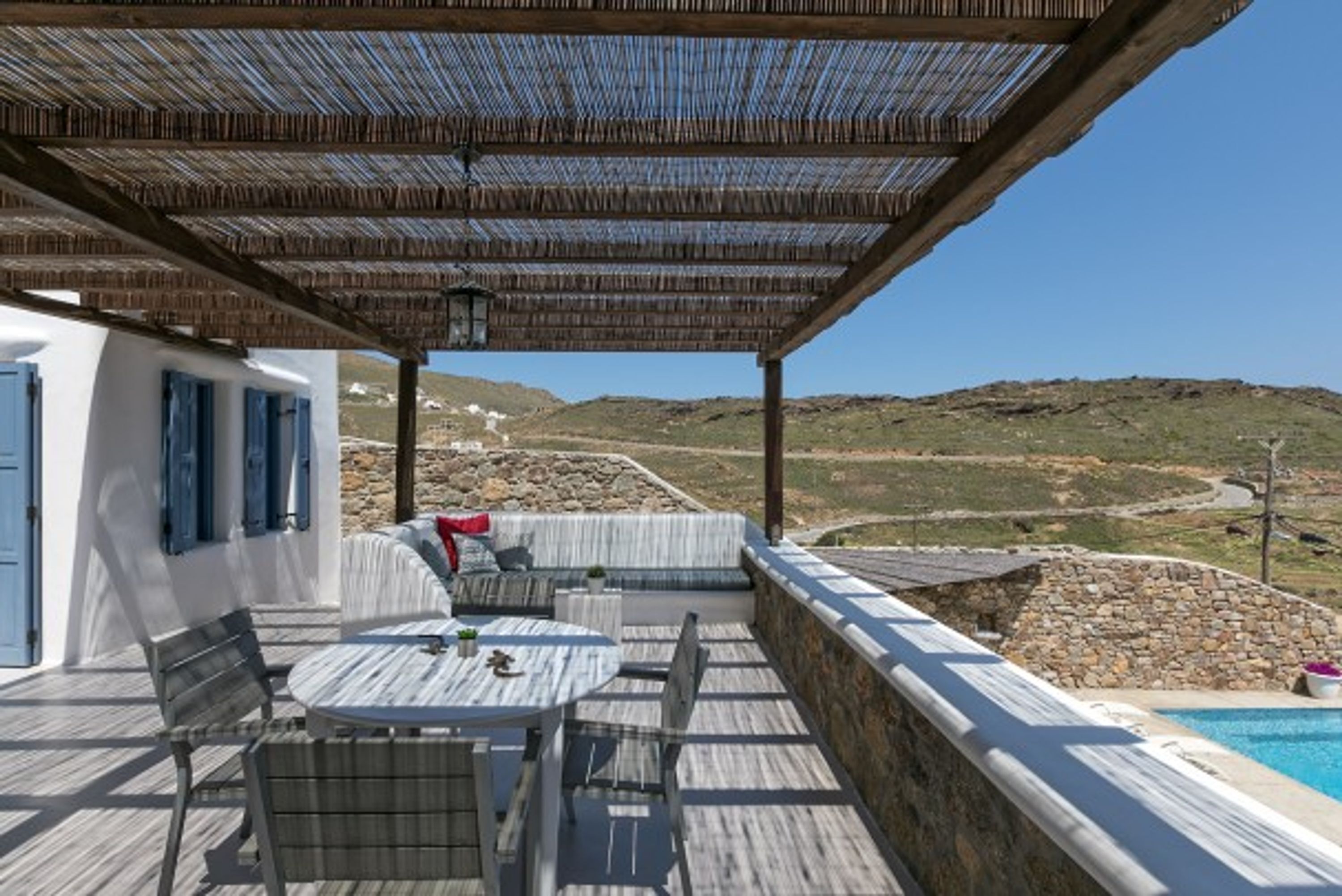 Un espacio al aire libre cubierto con mesa y sillas, con vista a una piscina y un paisaje montañoso.