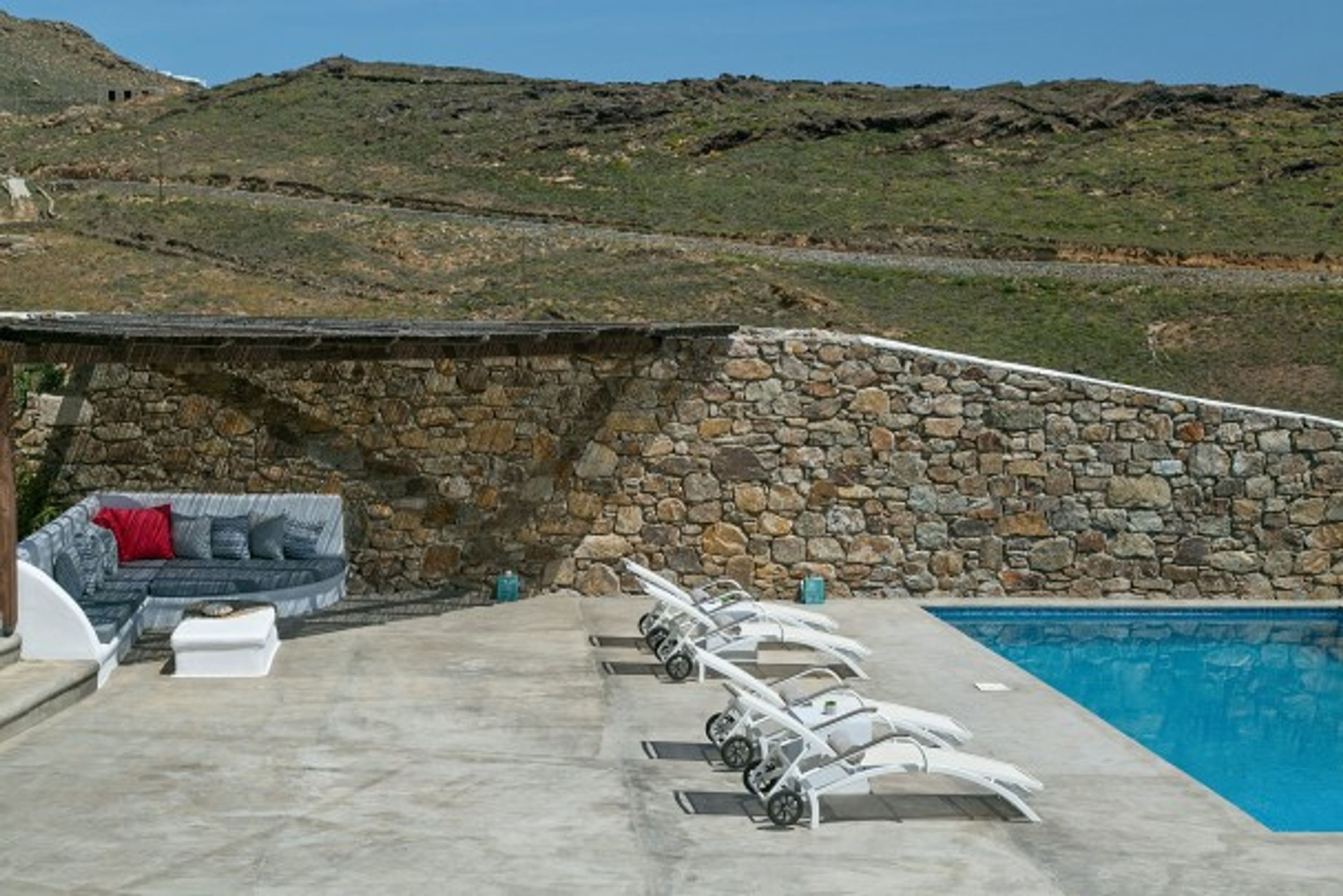 Ein Poolbereich mit einer Steinwand, einer Couch und Liegestühlen.