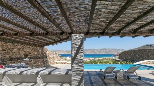 Uma área de estar coberta ao ar livre com piscina e vista para o mar.