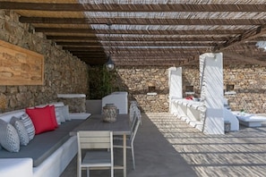 An outdoor patio with stone walls, a wooden ceiling, and a seating area with cushions and a table. - 4 Bedroom Villa with private pool and sea view (Mikonos)