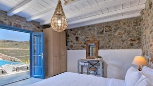 Um quarto com parede de pedra, guarda-roupa de madeira, uma escrivaninha e uma cama.