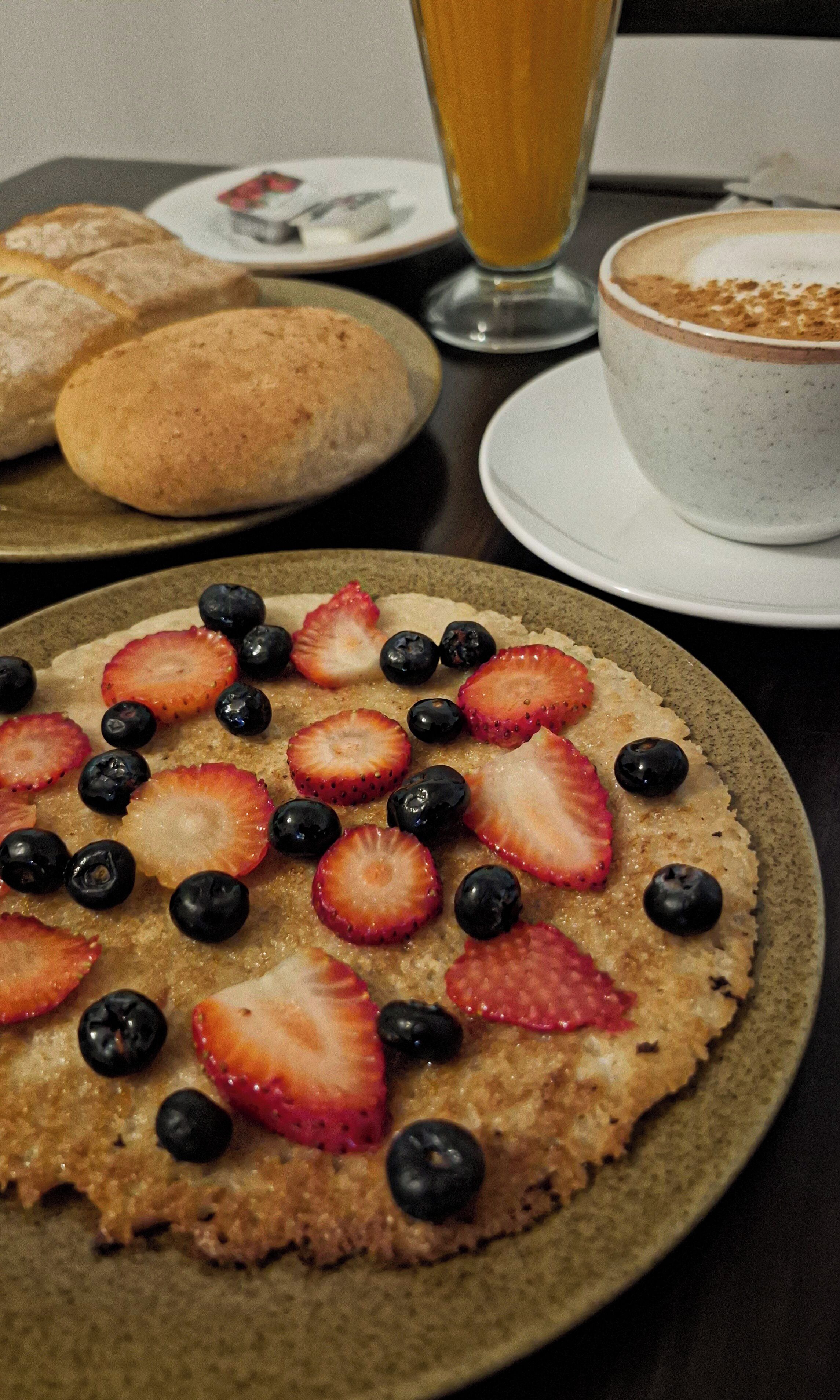 A breakfast setting with a plate of fruit-topped pancakes, a glass of orange juice, and a cup of coffee on a table.