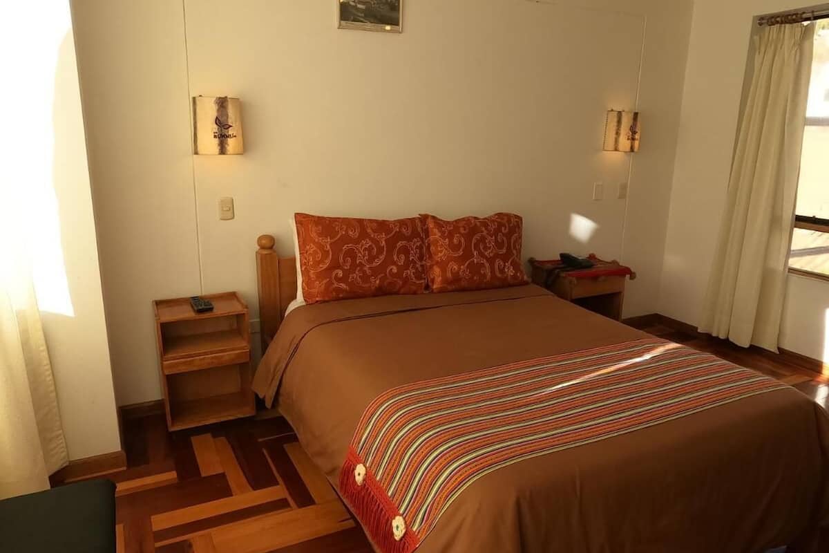 Habitación de hotel con una cama grande, dos mesitas de noche, una lámpara y un ventanal con cortinas.