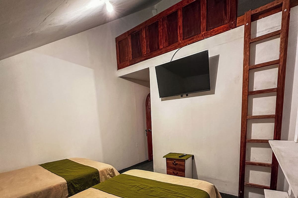 Habitación con dos camas, un televisor fijado a la pared, una escalera de madera y una mesita.