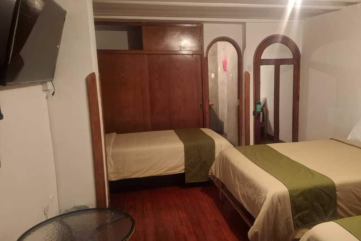 Una habitación con dos camas, un armario de madera, un televisor y un espejo.