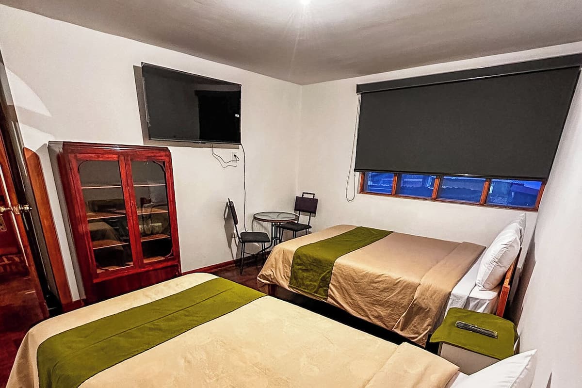 Una habitación con dos camas, una mesita, un armario y una ventana con vistas.