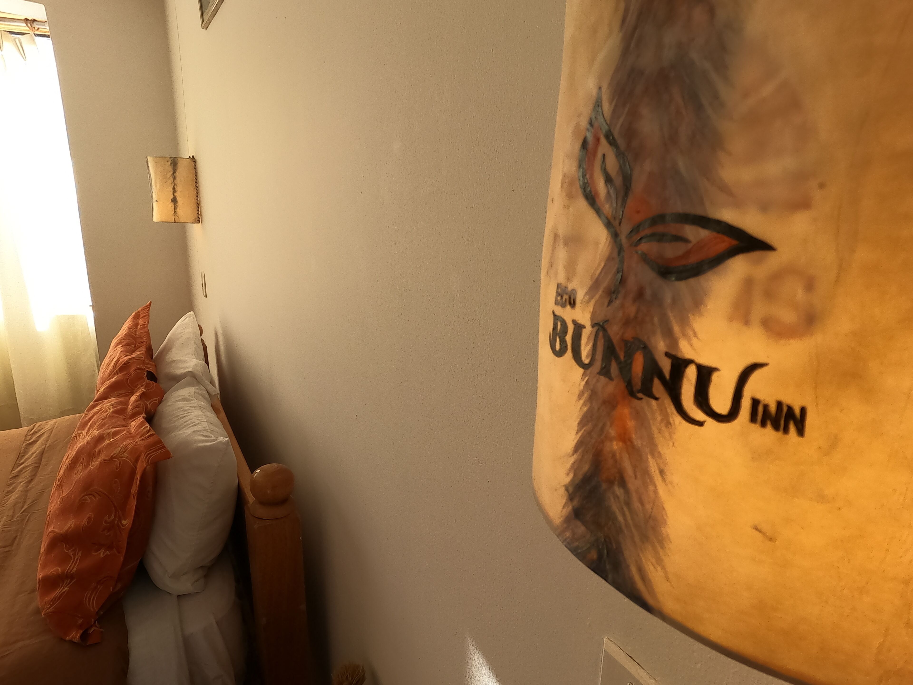A room with a bed, a pillow, a blanket, and a wall with a partial view of a mural.