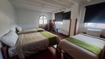 A room with two beds, a small table, a chair, a window with a blind, and a door with a window.