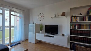 A living room with a TV, bookshelf, and a sliding glass door to a balcony. - Beachfront, 2-room apartment on the 1st floor with WLAN (Graal-Müritz)