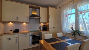 A modern kitchen with built-in appliances, a dining area with a table and chairs, and a window with curtains. - Beachfront, 2-room apartment on the 1st floor with WLAN (Graal-Müritz)