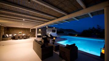 Un área de piscina al aire libre con mobiliario de mimbre, un muro de piedra y vistas a la piscina al atardecer.