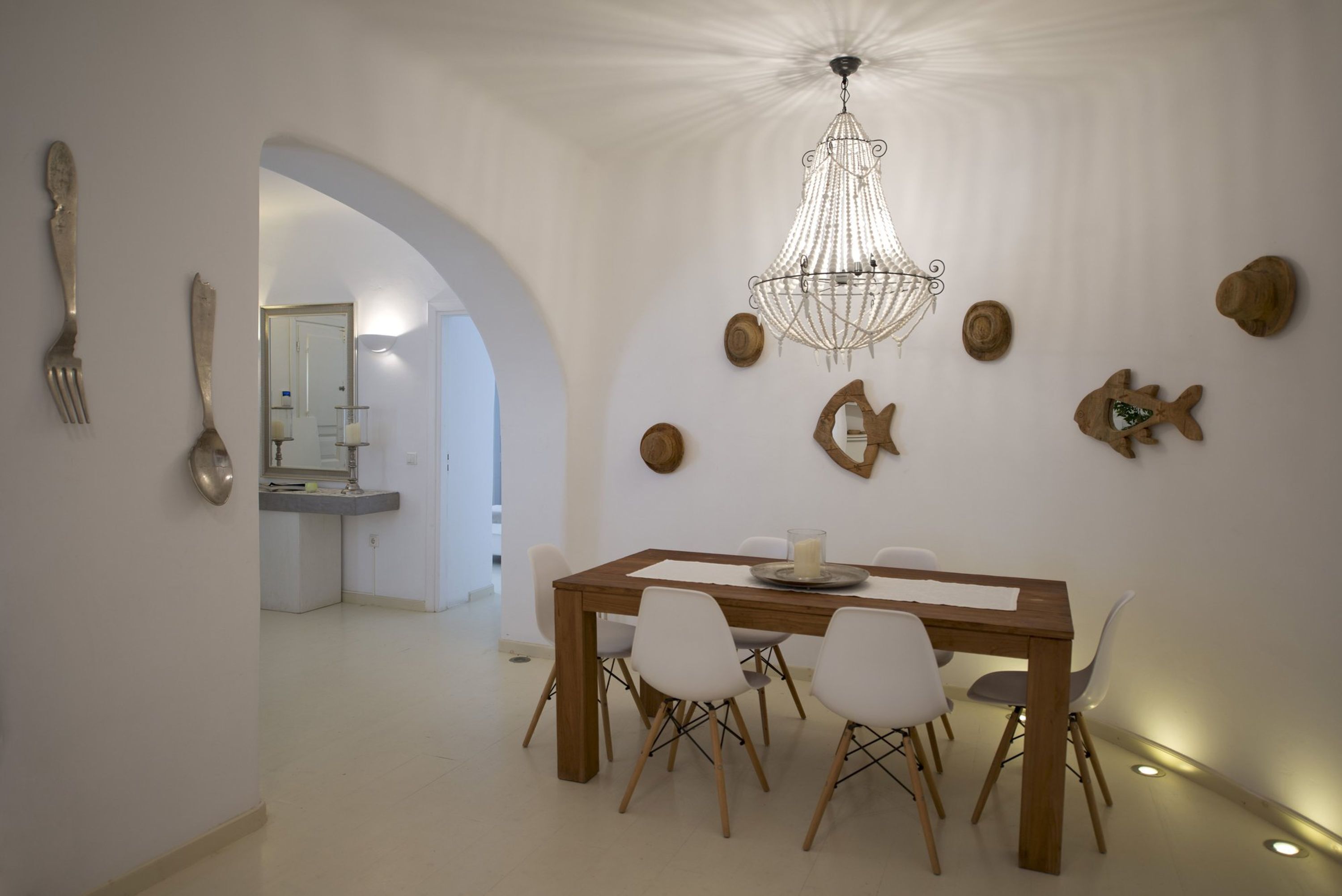 Un comedor con una mesa de madera, sillas blancas y una araña.