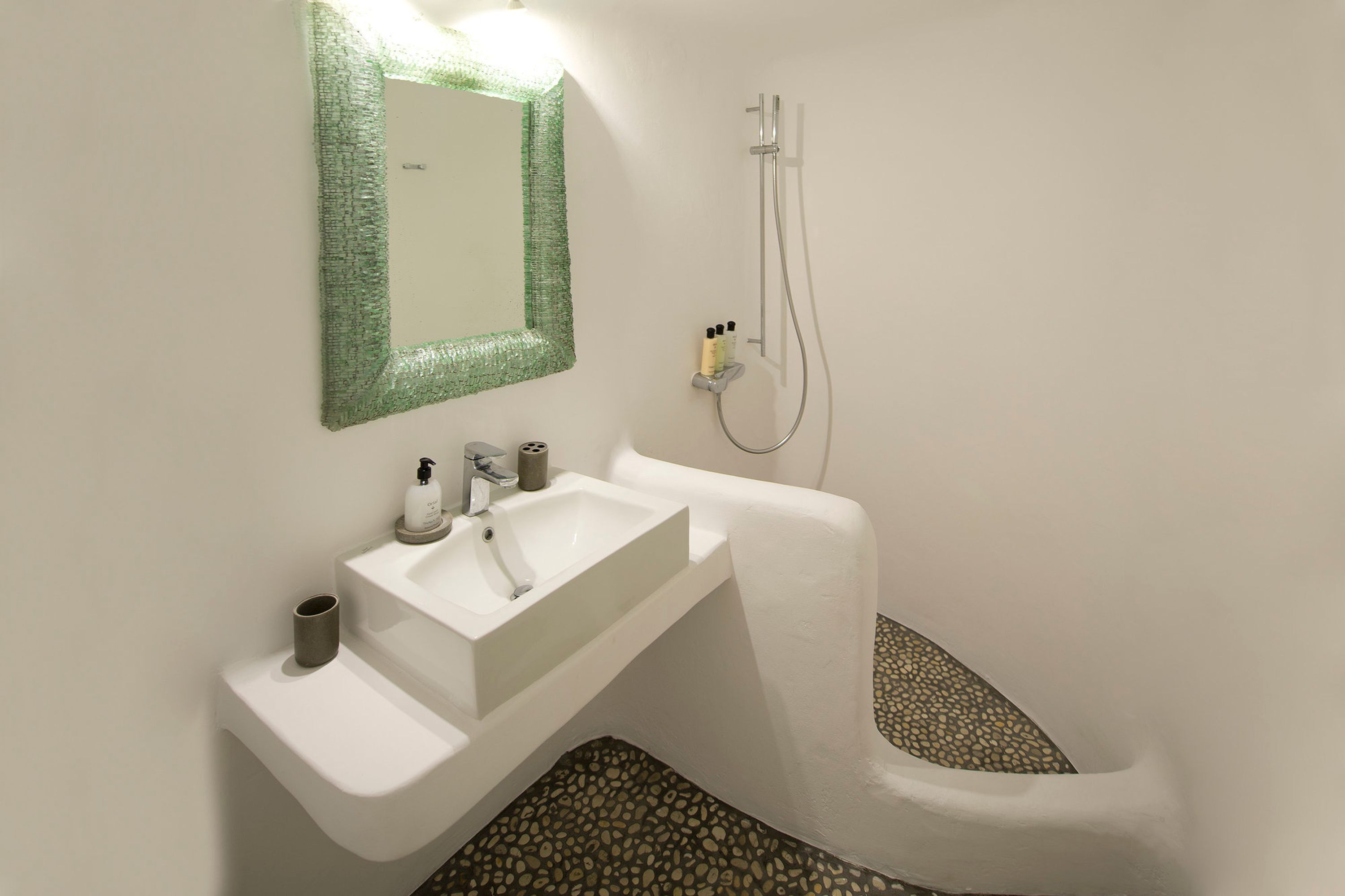 A bathroom with a white sink, a mirror with a green frame, a shower, and a tiled floor.