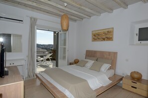 Une chambre à coucher avec un lit, des tables de chevet, une télévision, une fenêtre donnant sur un beau paysage et un tableau accroché au mur.