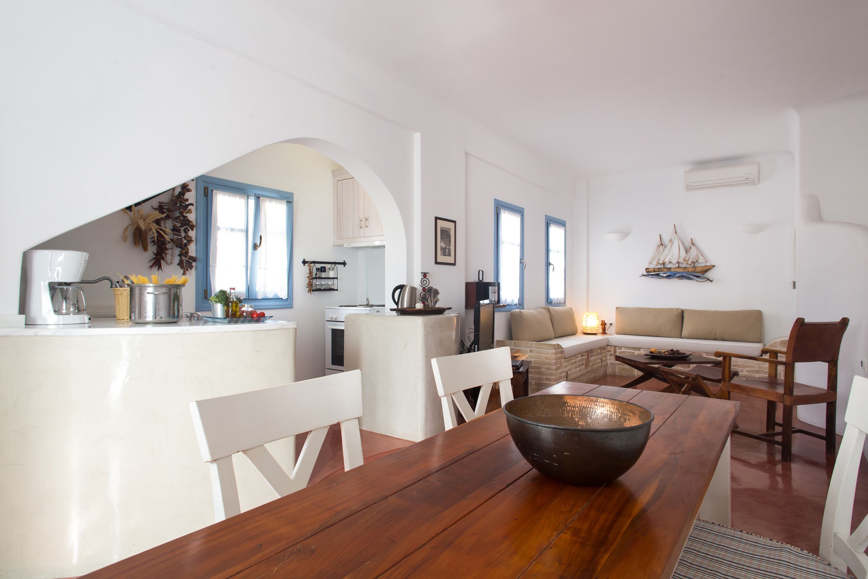 Eine moderne Küche mit weißen Schränken, ein Essbereich mit einem Holztisch und Stühlen, sowie ein Wohnbereich mit einer Couch und einer kleinen Schiffdekoration an der Wand.