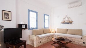 A living room with a TV, a stone bench, a wooden coffee table, and a wall-mounted ship decoration. - Daphne - Two Bedroom Villa, private pool, sea view (Agia Paraskevi)