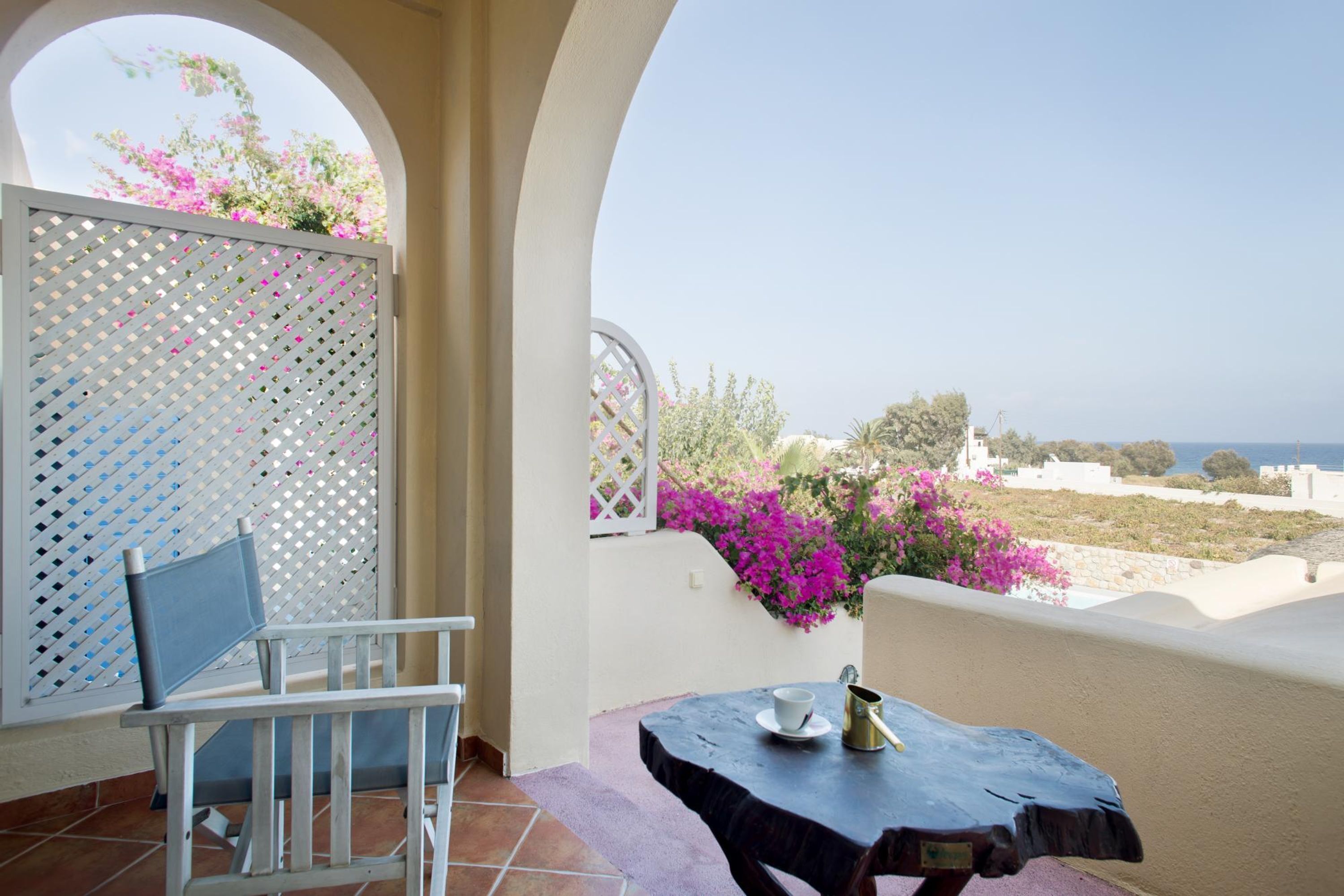 Ein Balkon mit Tisch und Stuhl, Blick auf das Meer und rosa Blüten.