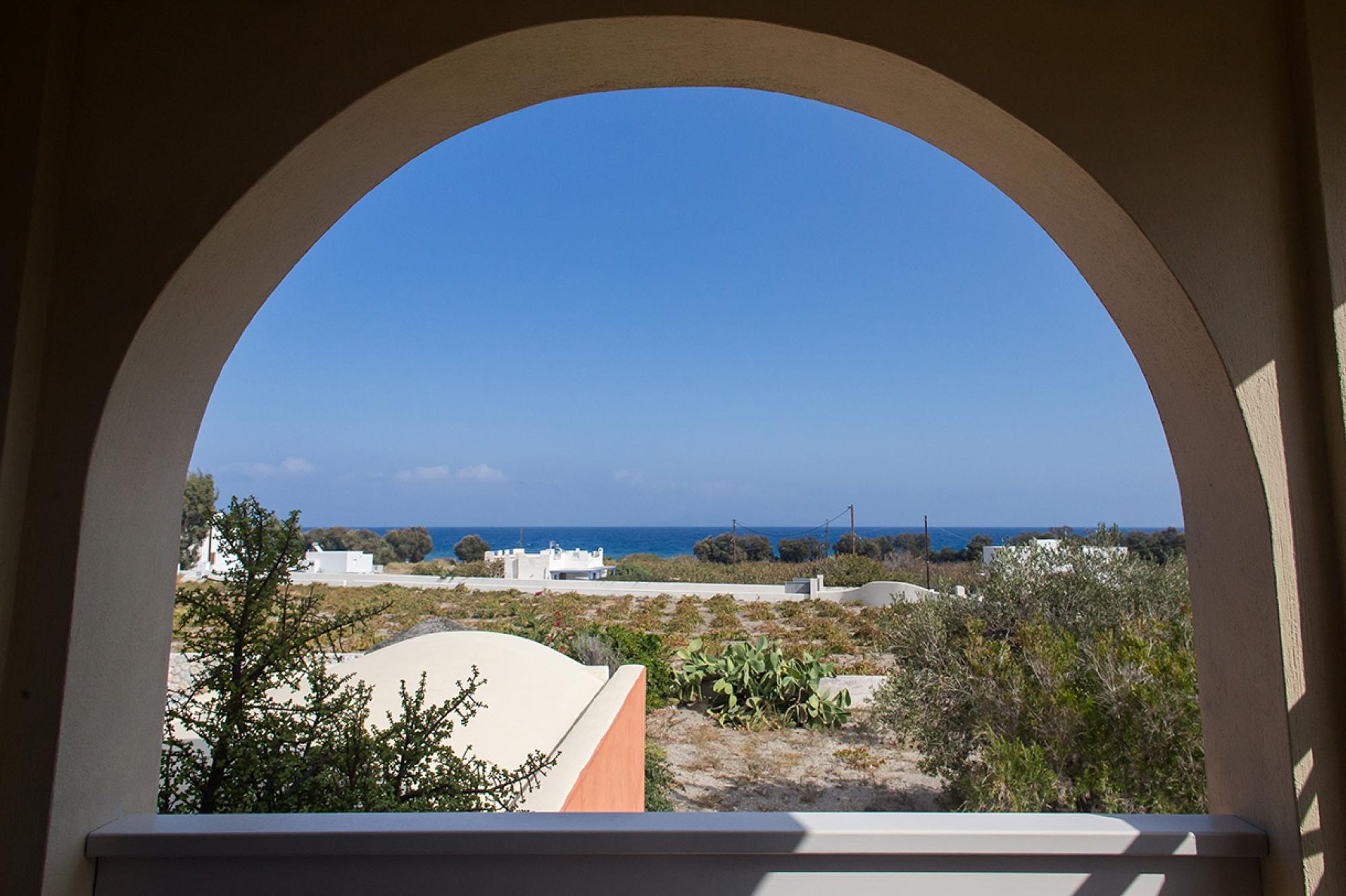 Une vue à travers une fenêtre en arc donnant sur un paysage côtier, avec des bâtiments et de la végétation.