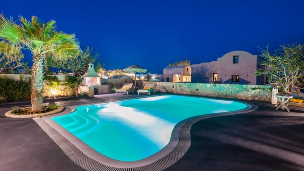 A swimming pool with a curved edge, surrounded by a stone wall and palm trees. - Daphne - Two Bedroom Villa, private pool, sea view (Agia Paraskevi)
